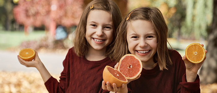 Zwei lachende Mädchen halten Zitrusfrüchte in herbstlicher Umgebung